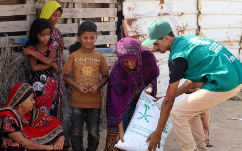 A male volunteer giving a group of women and children food aid.